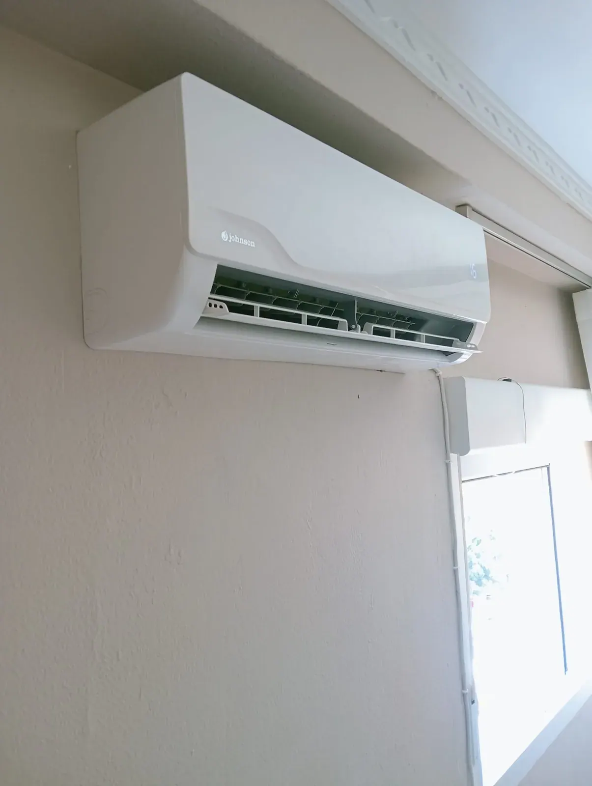 Unidad interior de aire acondicionado split instalada en la pared junto a una ventana