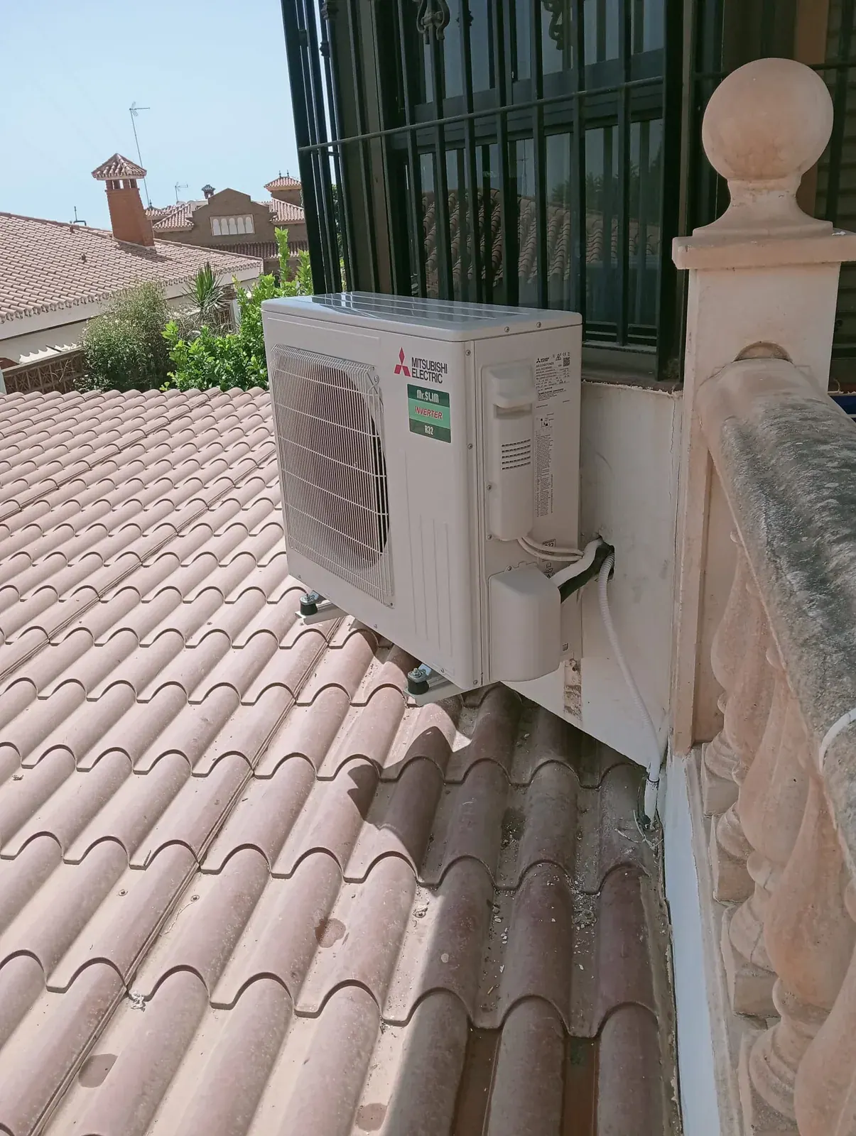Unidad exterior de aire acondicionado montada sobre soportes de pared junto al tejado de una vivienda