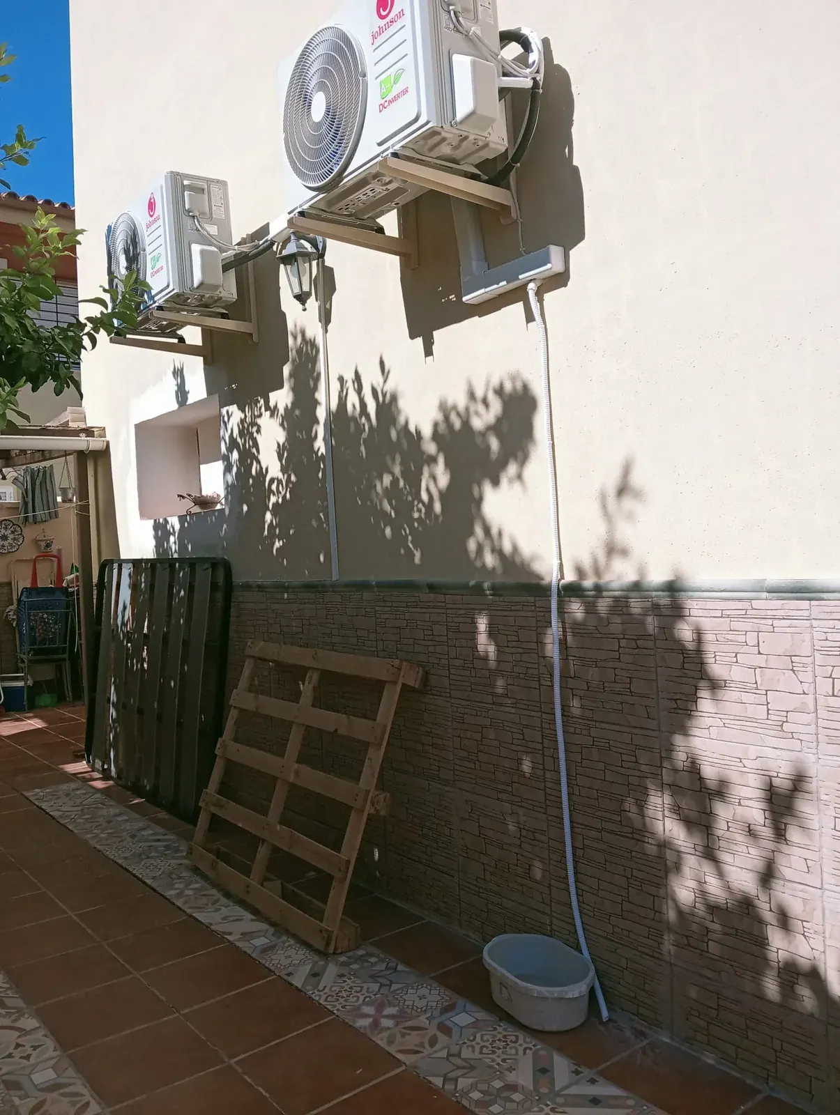 Dos unidades exteriores de aire acondicionado montadas sobre soportes de pared en el patio de una vivienda